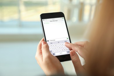 Woman writing message with text I Love You on smartphone against blurred background, closeup