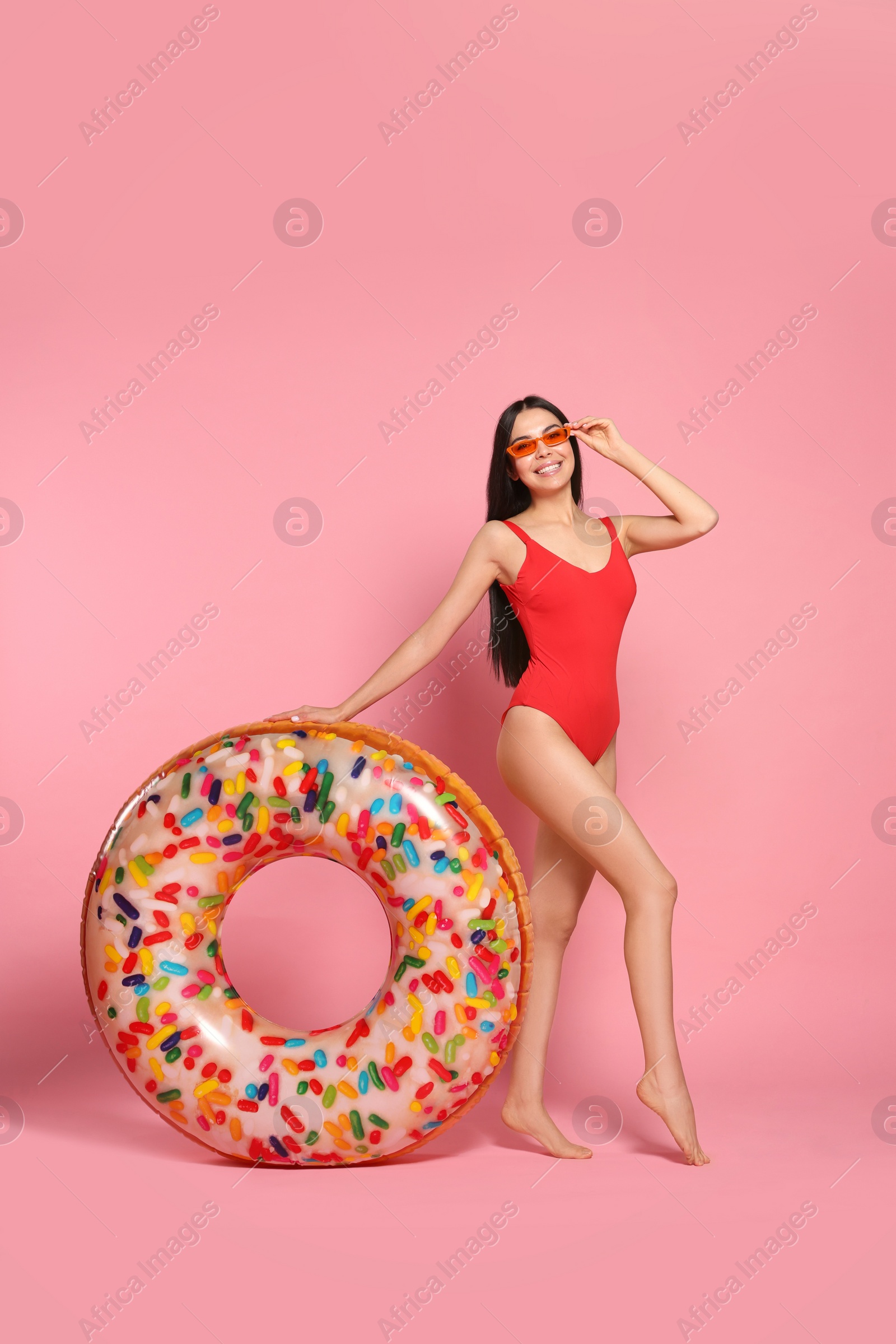 Photo of Young woman with stylish sunglasses holding inflatable ring against pink background