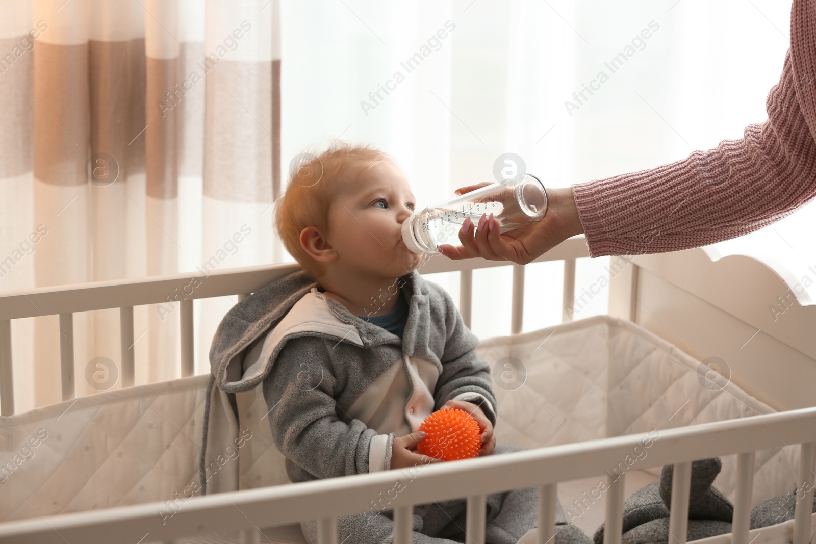 Photo of Nanny giving cute little baby water from bottle at home