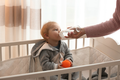 Nanny giving cute little baby water from bottle at home