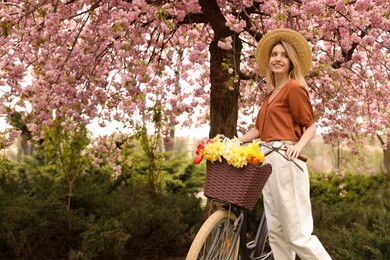 Photo of Beautiful young woman with bicycle and flowers in park on pleasant spring day. Space for text