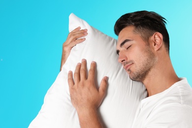 Young man with soft pillow on color background