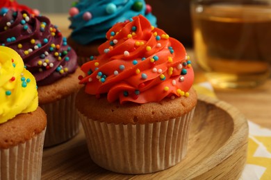 Photo of Delicious cupcakes with colorful cream and sprinkles on wooden board, closeup