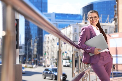 Beautiful businesswoman with laptop in city on sunny day