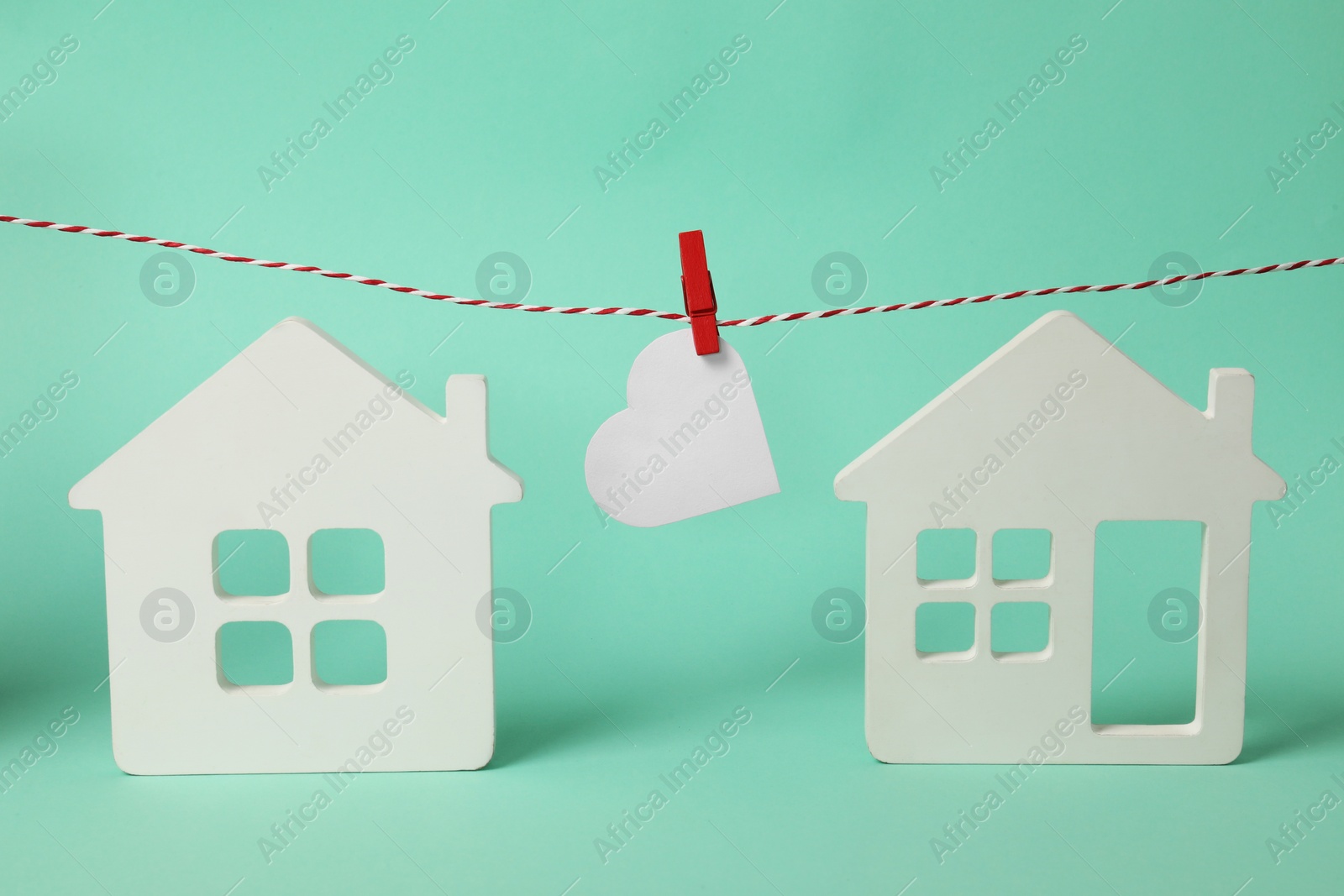 Photo of Long-distance relationship concept. Paper heart hanging on decorative cord between two white house models against turquoise background