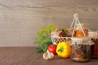 Composition with jars of tasty pickled vegetables on brown table. Space for text