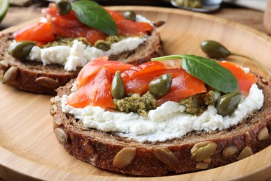 Photo of Delicious sandwiches with cream cheese, salmon, capers and pesto on wooden plate, closeup