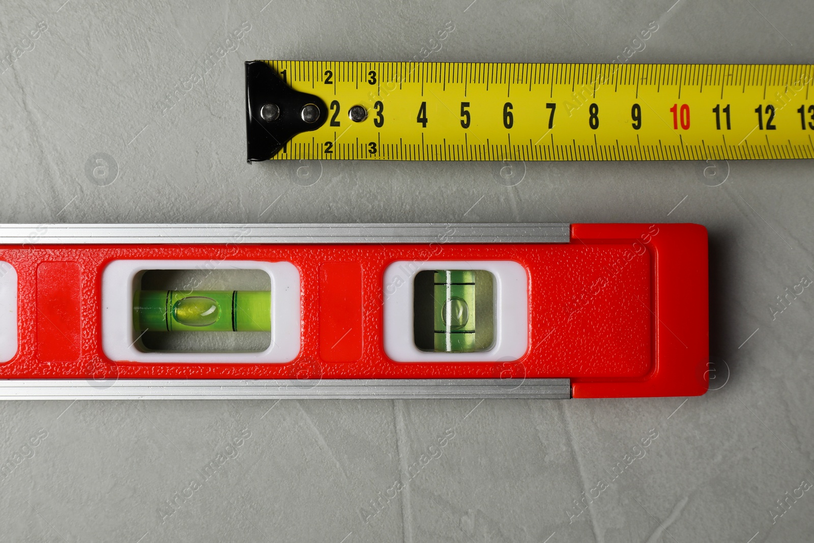 Photo of Building level and tape measure on grey table, top view