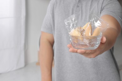 Man holding tasty fortune cookies with predictions indoors, closeup. Space for text