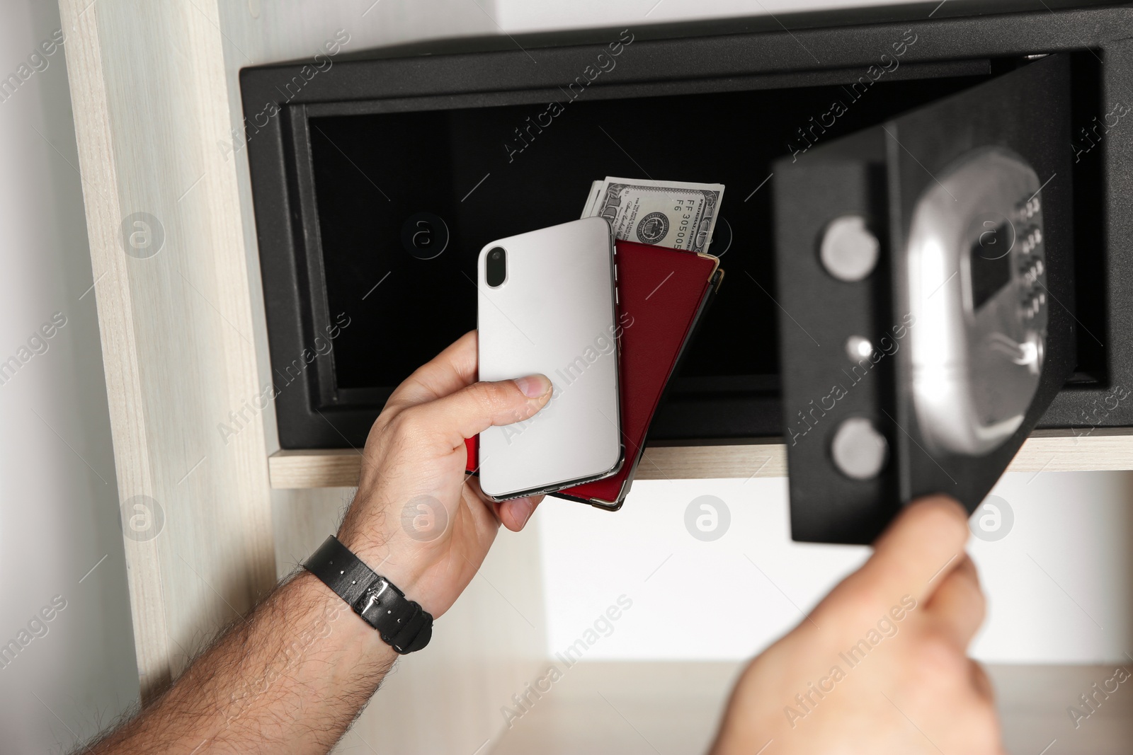 Photo of Man putting smartphone, passport and money into steel safe, closeup