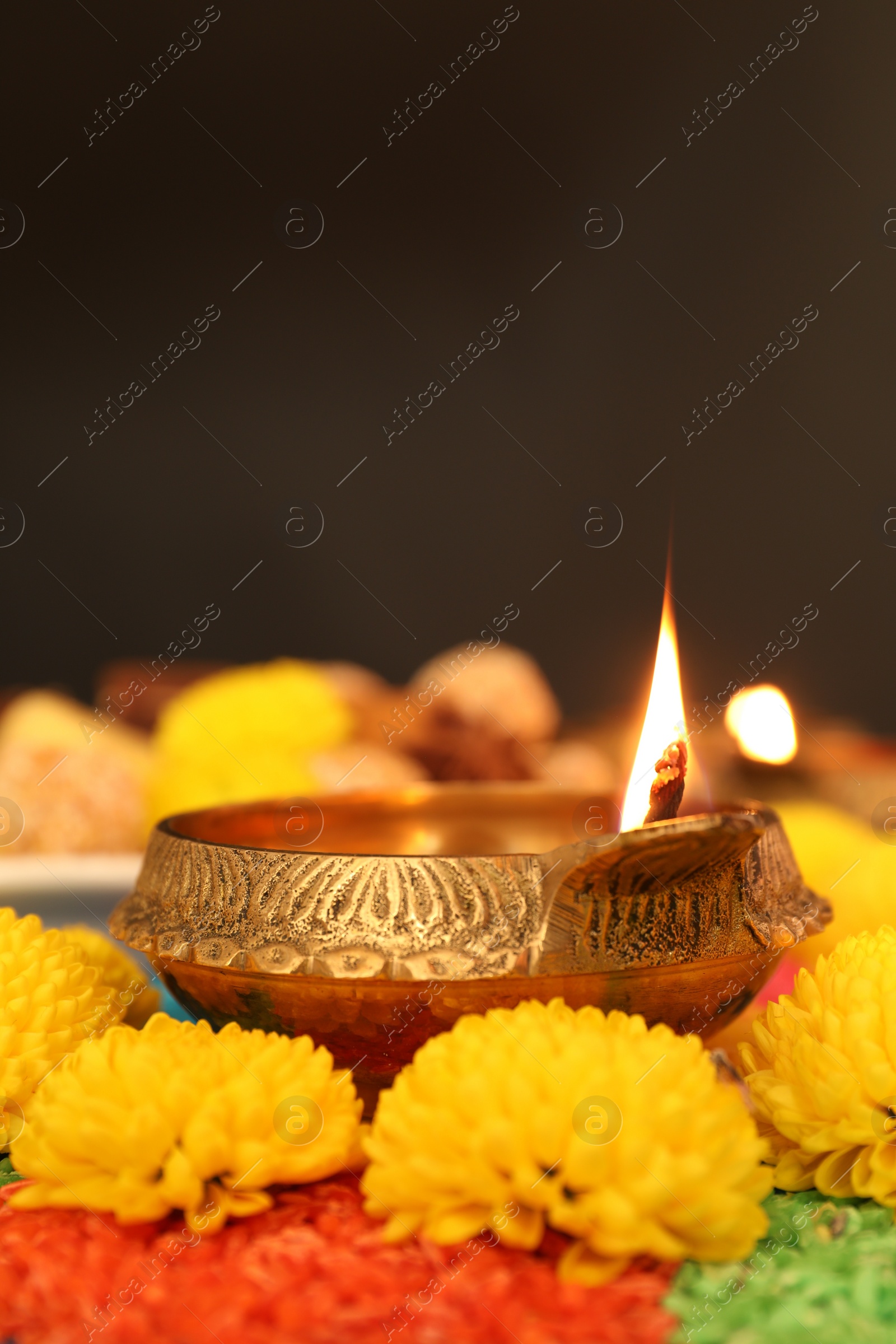 Photo of Diwali celebration. Diya lamp, colorful rangoli and chrysanthemum flowers on table against dark background, closeup. Space for text