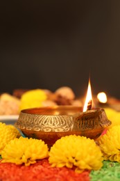 Photo of Diwali celebration. Diya lamp, colorful rangoli and chrysanthemum flowers on table against dark background, closeup. Space for text