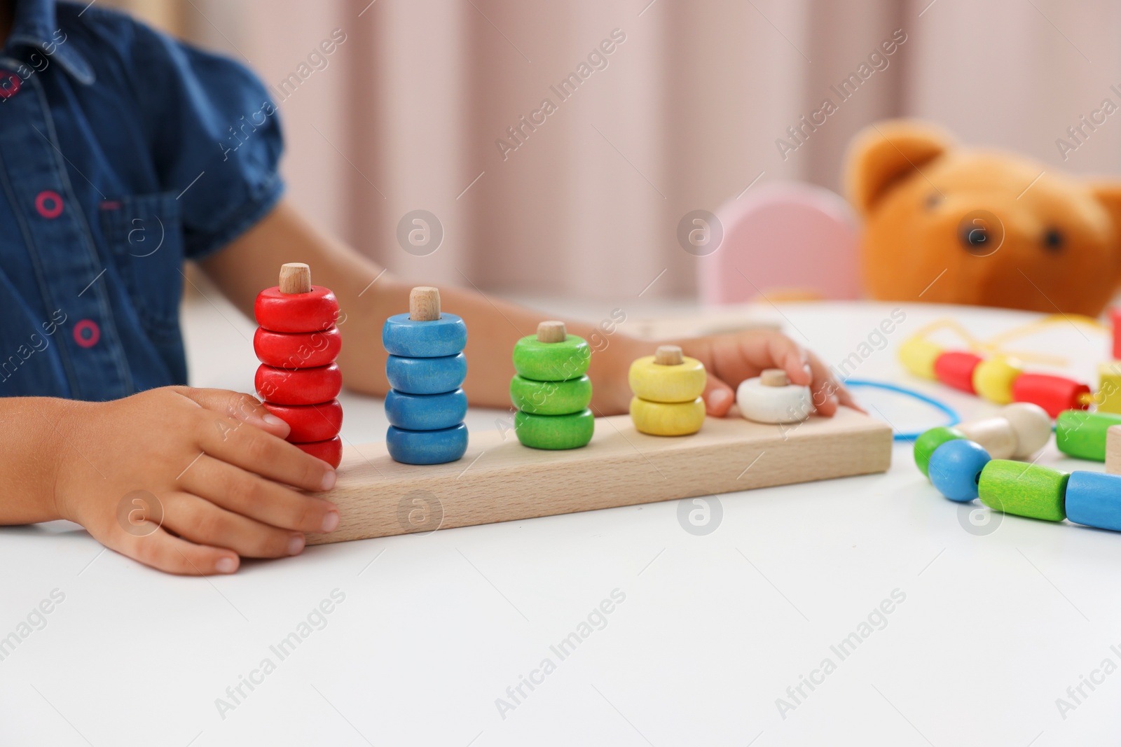 Photo of Motor skills development. Little girl playing with stacking and counting game at table indoors, closeup