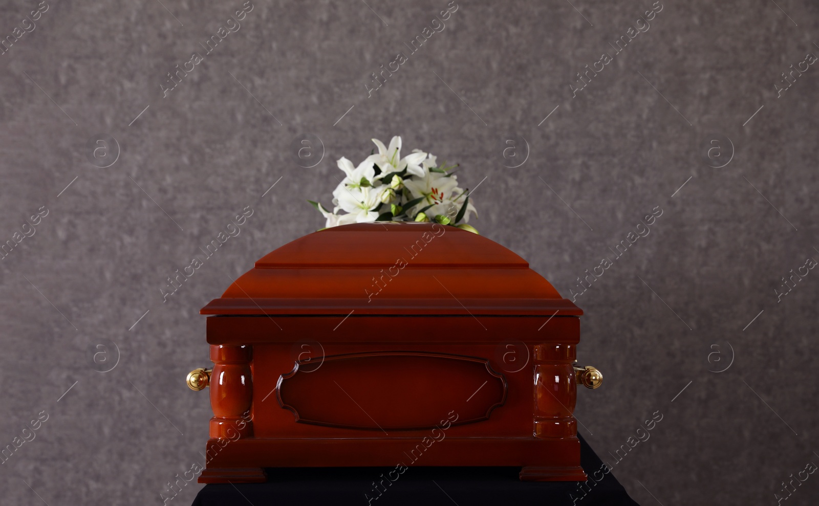 Photo of Wooden funeral casket with white lilies at grey wall