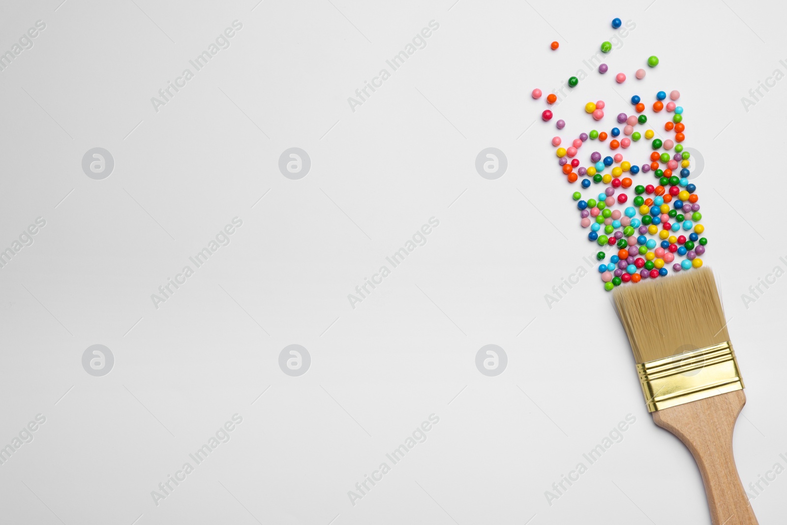 Photo of Brush painting with colorful sprinkles on light background, top view. Space for text. Creative concept