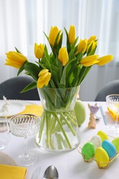 Festive table setting with glasses, painted eggs and vase of tulips. Easter celebration