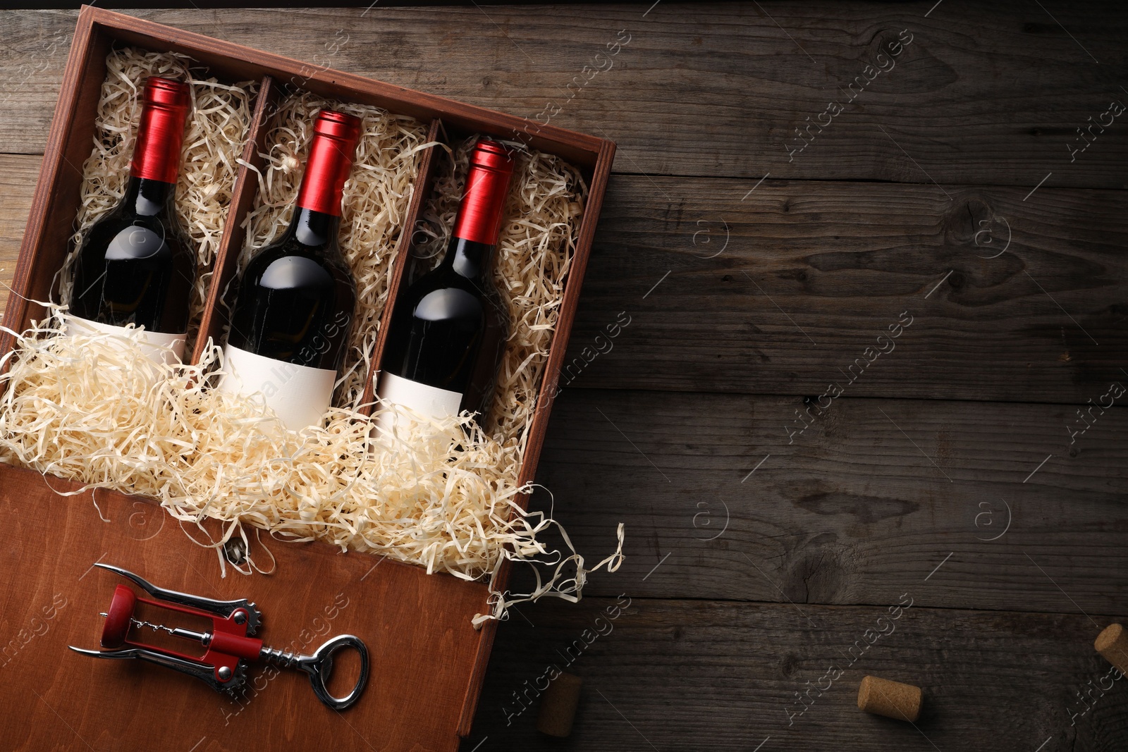 Photo of Box with wine bottles, corkscrew and corks on wooden table, flat lay. Space for text