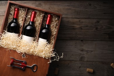 Box with wine bottles, corkscrew and corks on wooden table, flat lay. Space for text