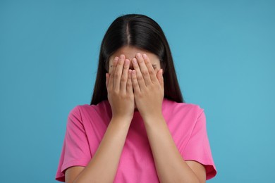 Resentful woman covering face with hands on light blue background