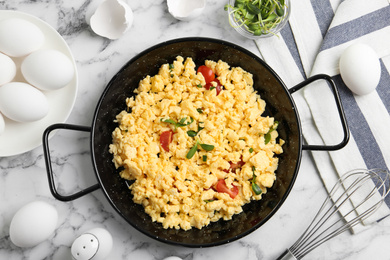 Tasty scrambled eggs with sprouts and cherry tomato in wok pan on white marble table, flat lay