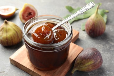 Photo of Jar of tasty sweet jam and fresh figs on grey table