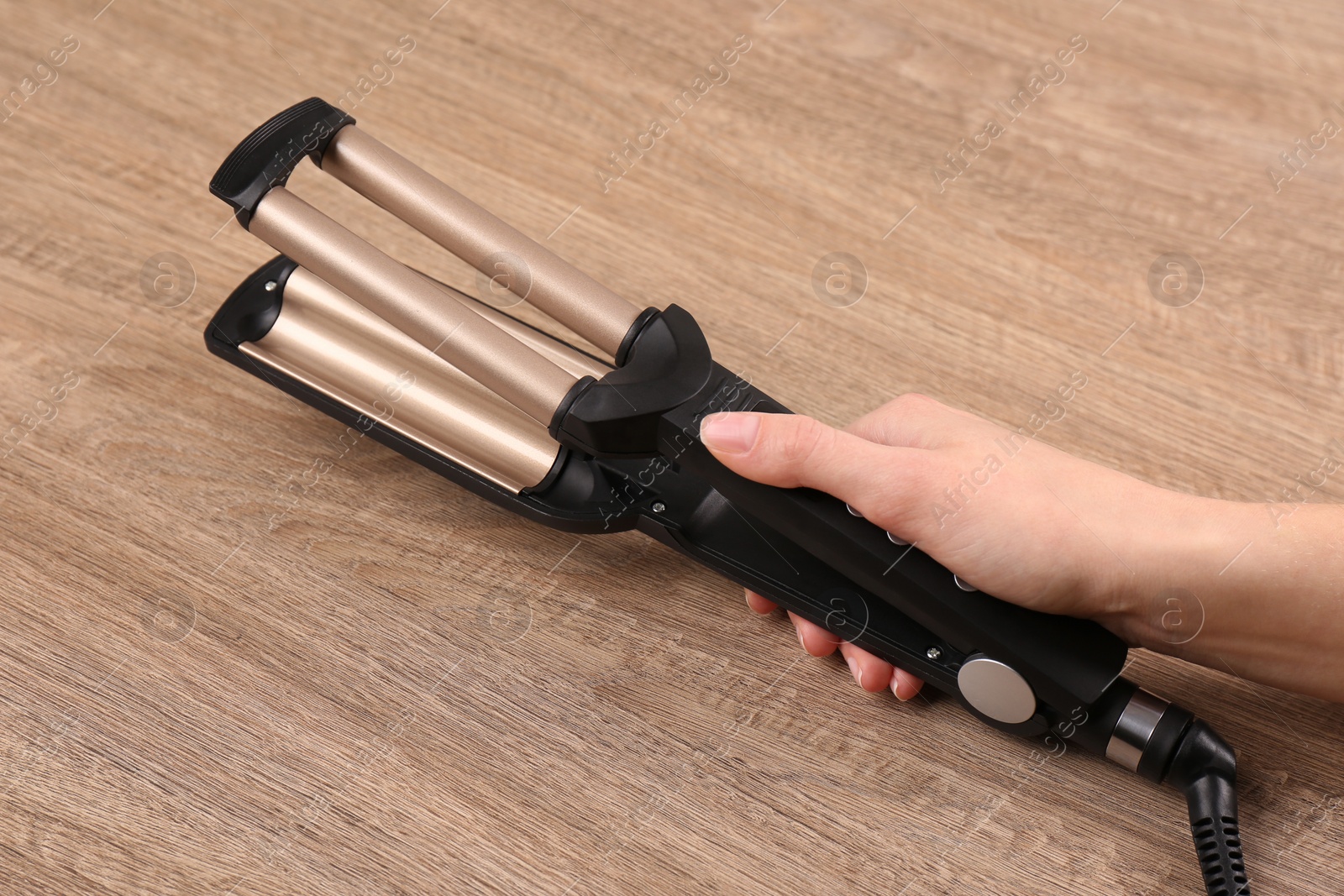 Photo of Woman holding modern triple curling iron on wooden background, closeup