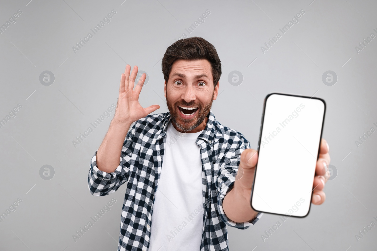 Photo of Surprised man showing smartphone in hand on light grey background