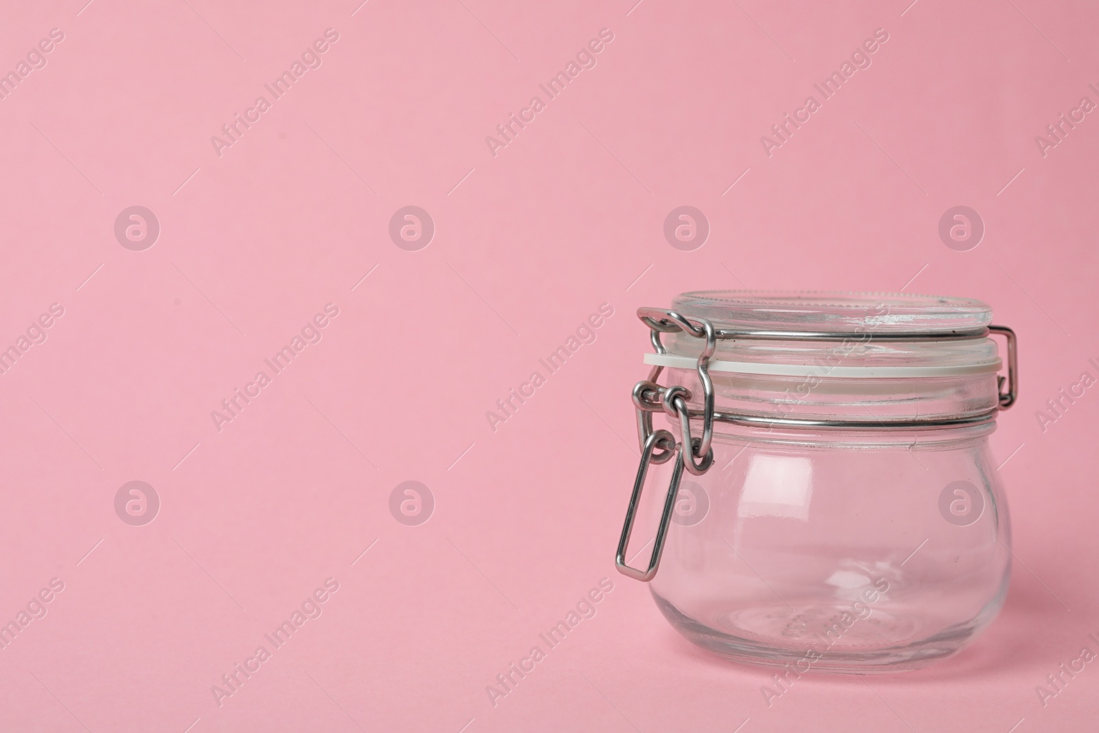 Photo of Closed empty glass jar on pink background, space for text