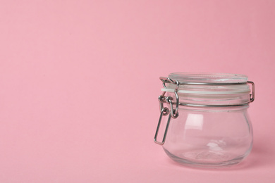 Photo of Closed empty glass jar on pink background, space for text