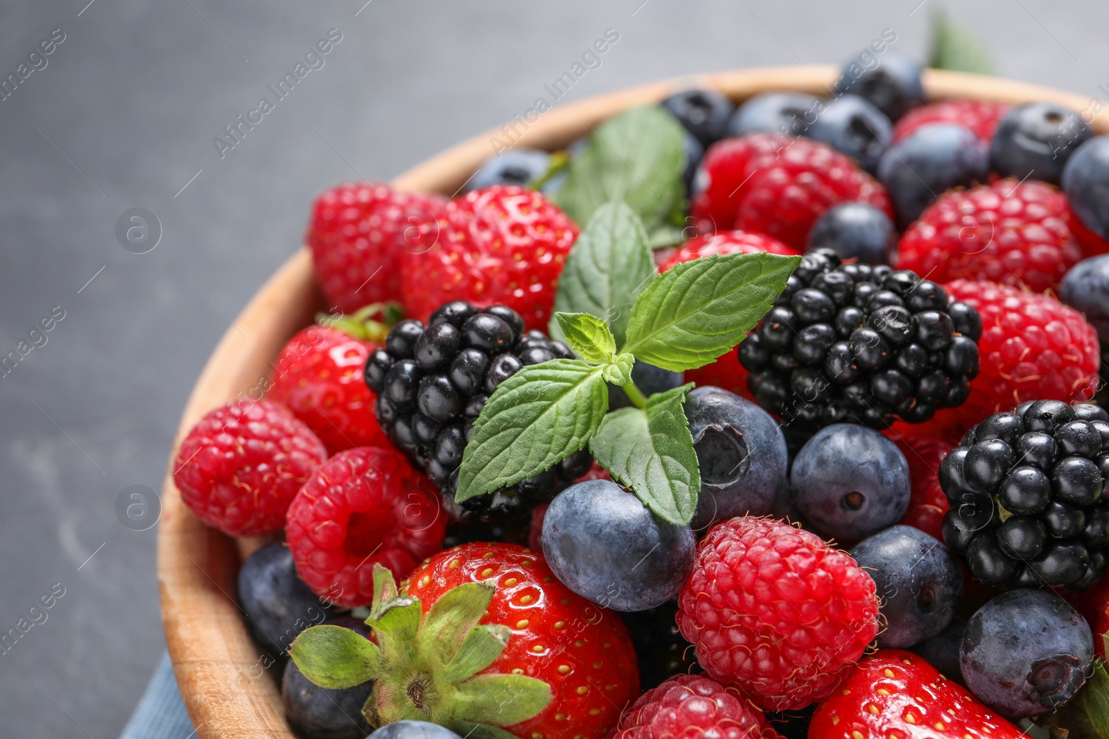 Photo of Many different fresh ripe berries in wooden bowl on black table, closeup