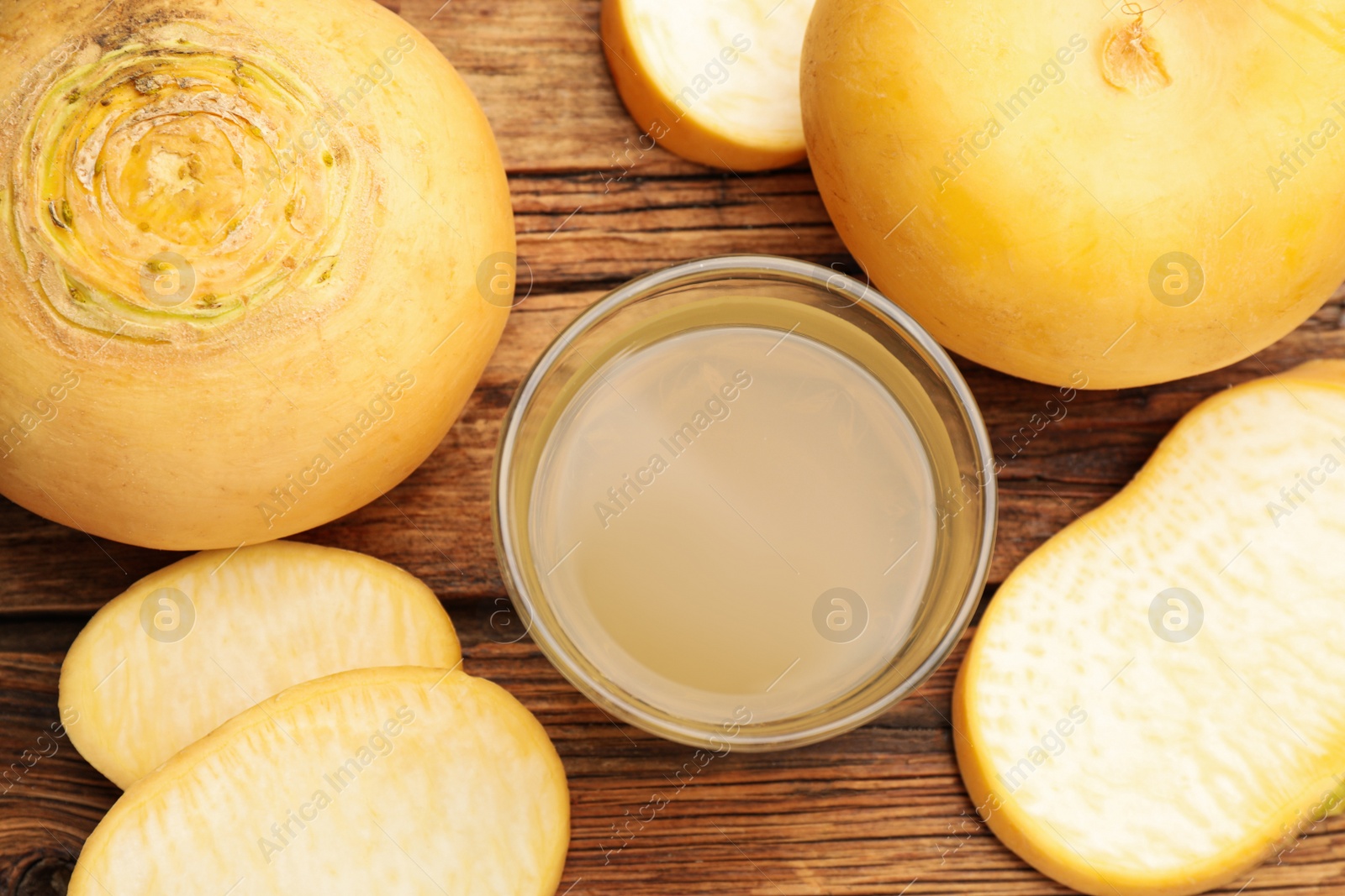 Photo of Glass of freshly made turnip juice on wooden table, flat lay