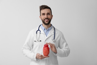 Photo of Doctor with stethoscope and model of heart on white background. Cardiology concept