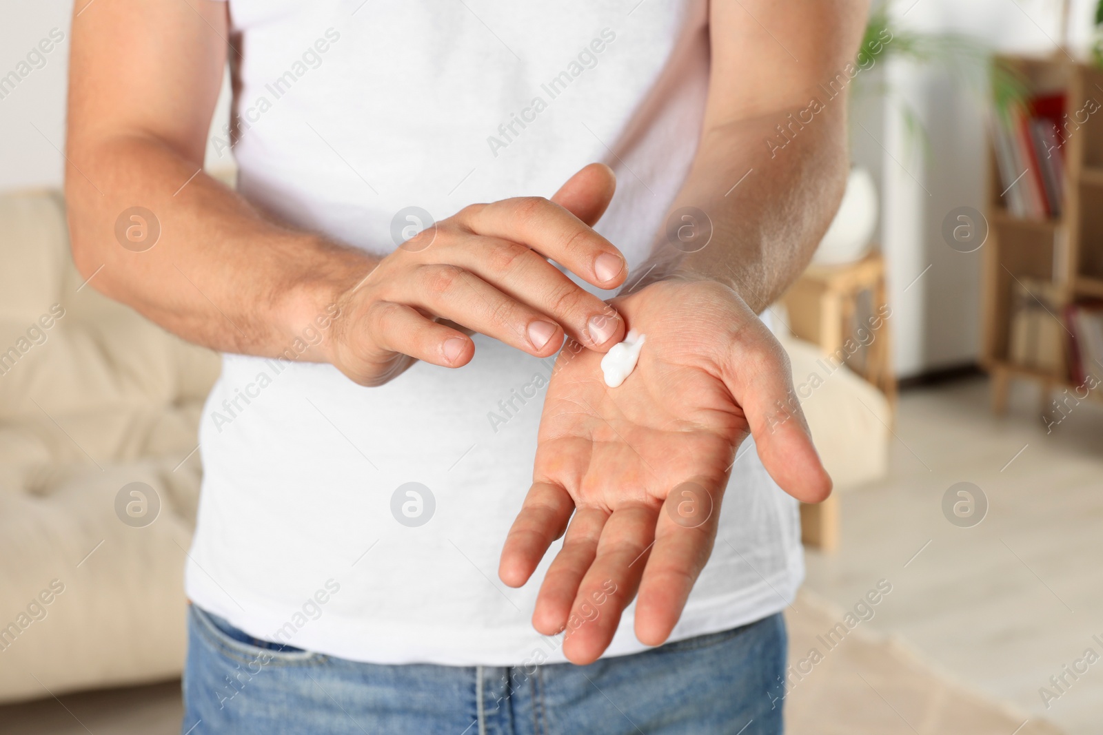 Photo of Man applying cream onto hand at home, closeup