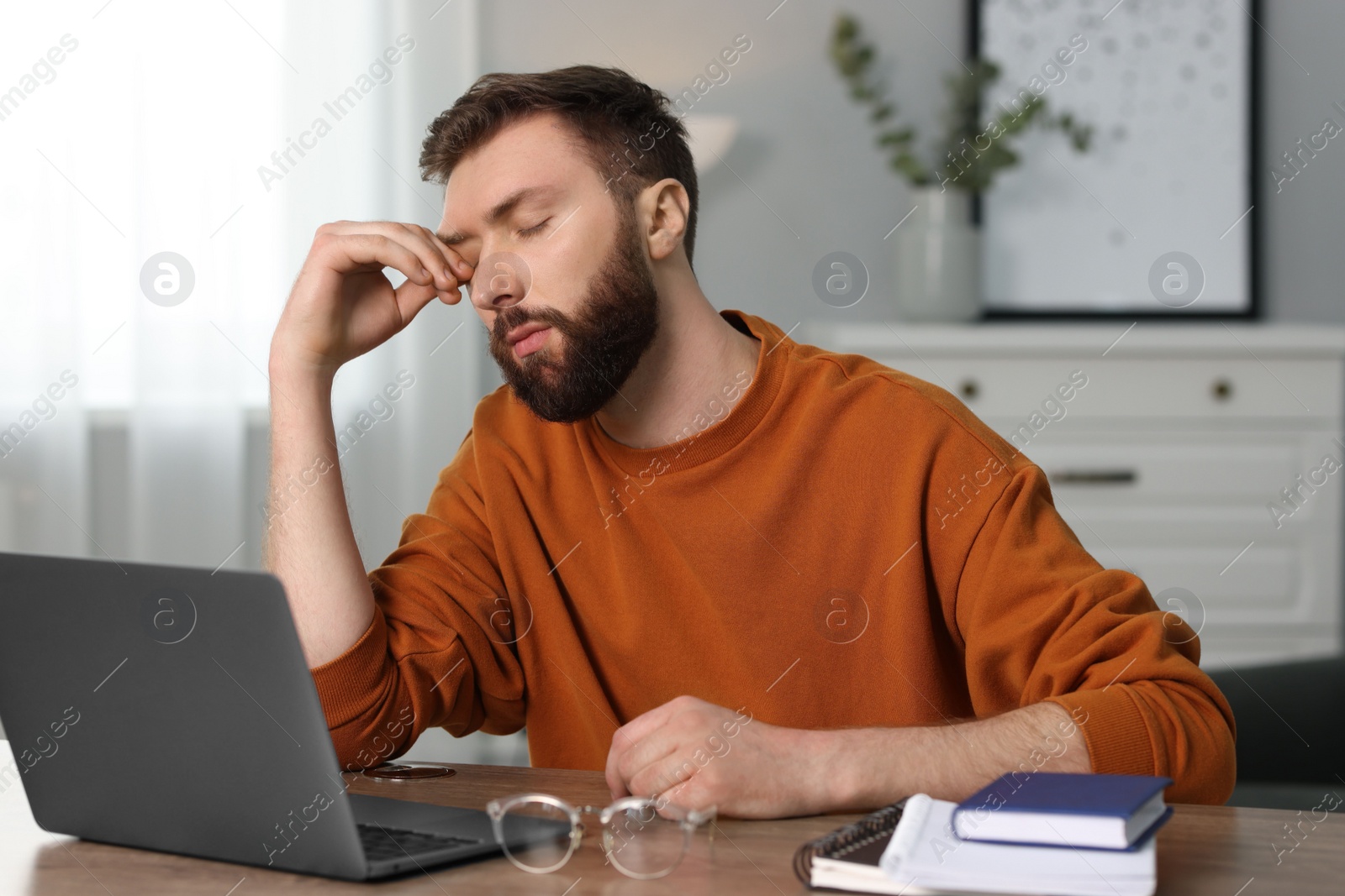 Photo of Overwhelmed man sitting with laptop at table indoors