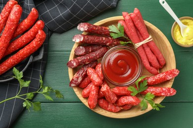 Photo of Different thin dry smoked sausages, parsley and sauces on green wooden table, flat lay