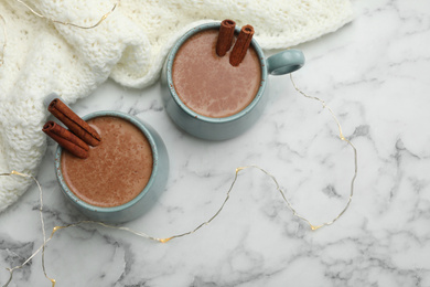 Photo of Cups of delicious hot cocoa with cinnamon on white marble table, flat lay. Space for text
