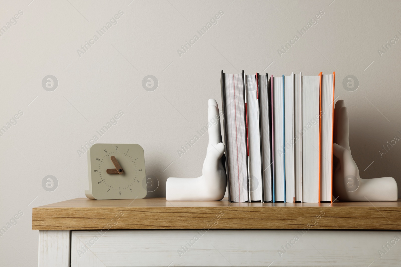 Photo of Beautiful hand shaped bookends with books and clock on table near light wall