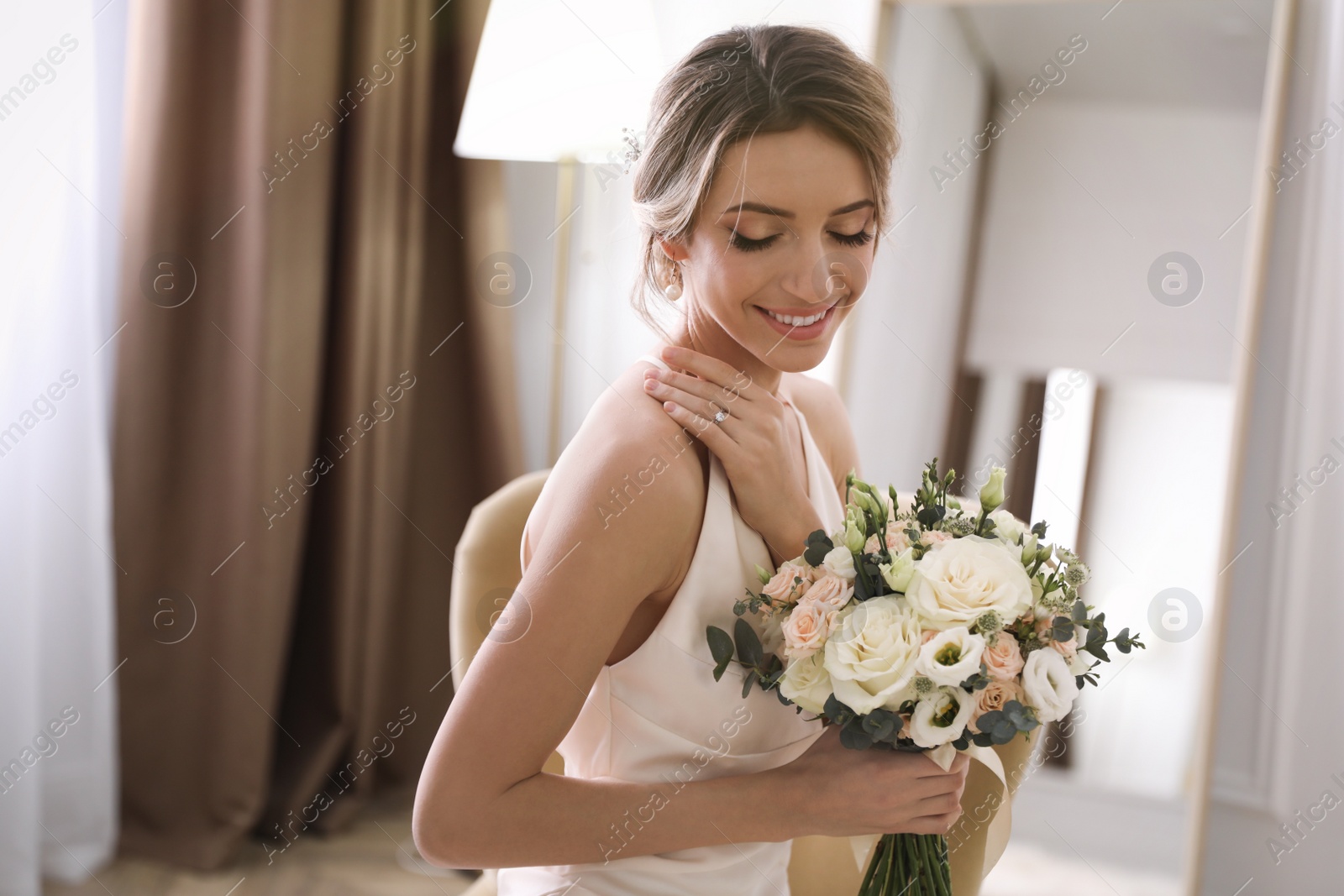 Photo of Beautiful young bride in elegant wedding dress with bouquet sitting in armchair