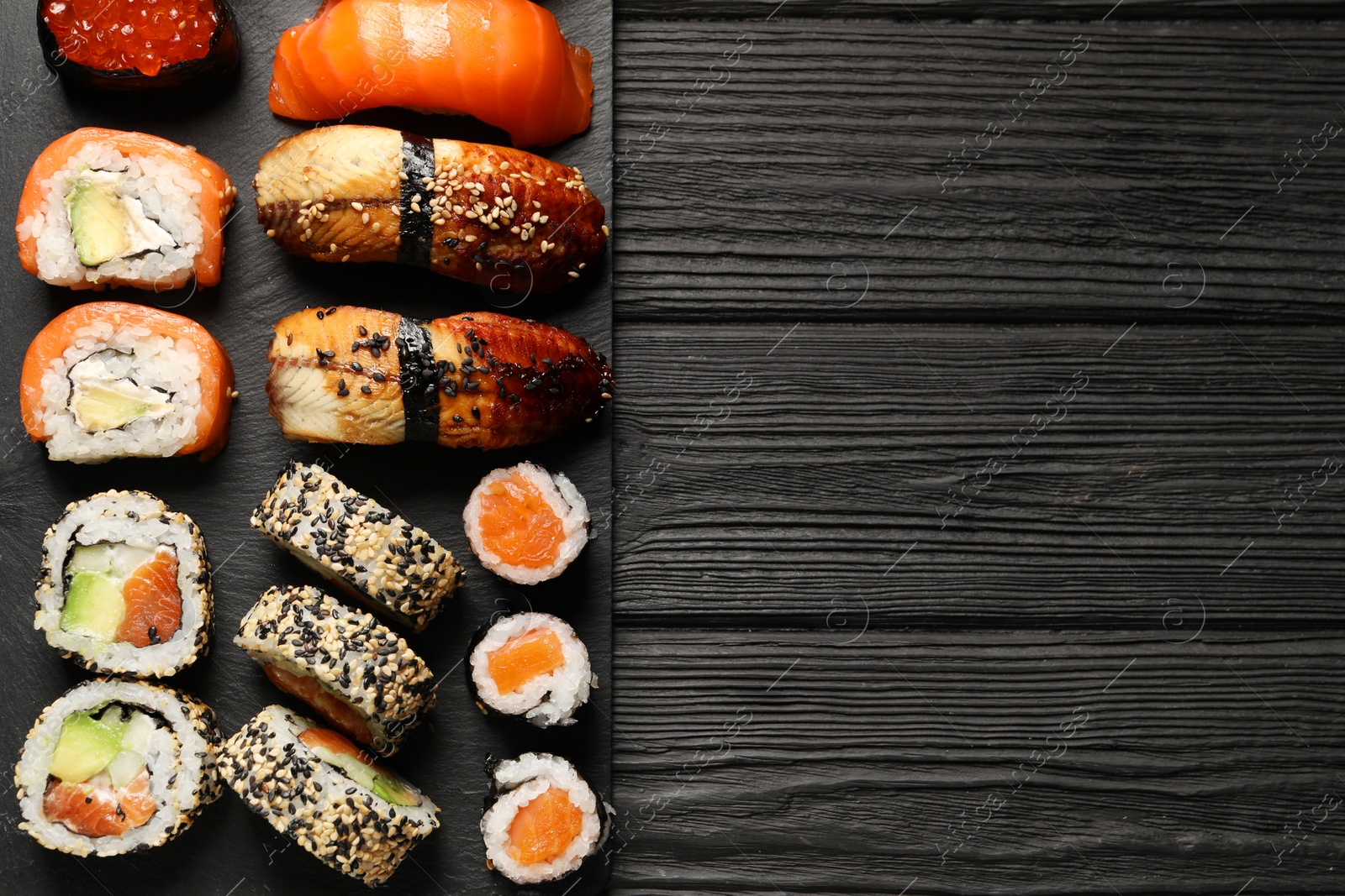 Photo of Set of delicious sushi rolls on black wooden table, top view. Space for text