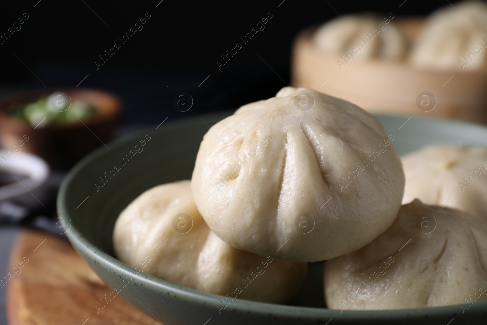 Photo of Delicious bao buns (baozi) in bowl on blurred background, closeup