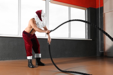 Photo of Young shirtless Santa Claus training with ropes in modern gym