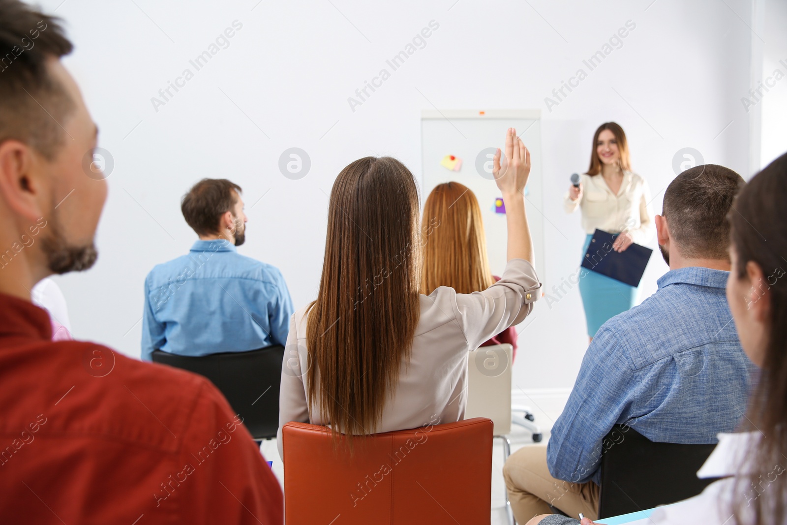 Photo of Young woman raising hand to ask question at business training indoors, back view