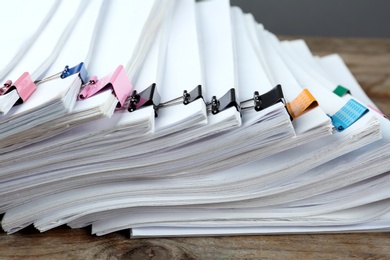 Stack of documents with colorful binder clips on wooden table, closeup
