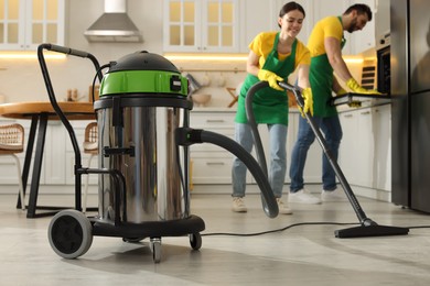 Photo of Professional janitors working in kitchen, focus on vacuum cleaner