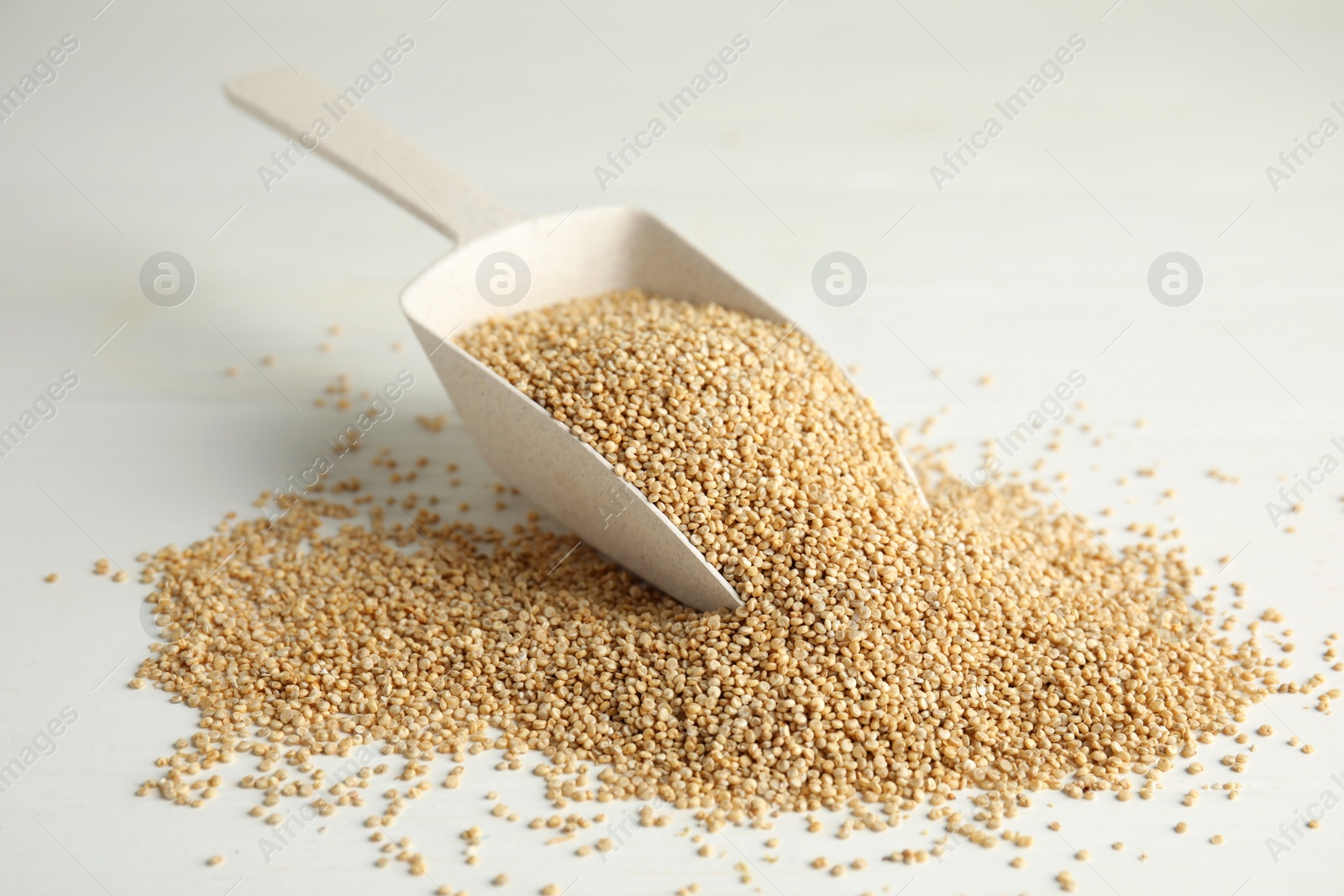 Photo of Scoop with uncooked quinoa on white table