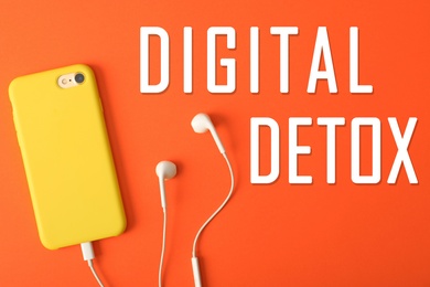 Image of Text Digital Detox, modern phone with earphones on bright orange background, top view