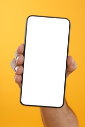 Man holding smartphone with blank screen on yellow background, closeup