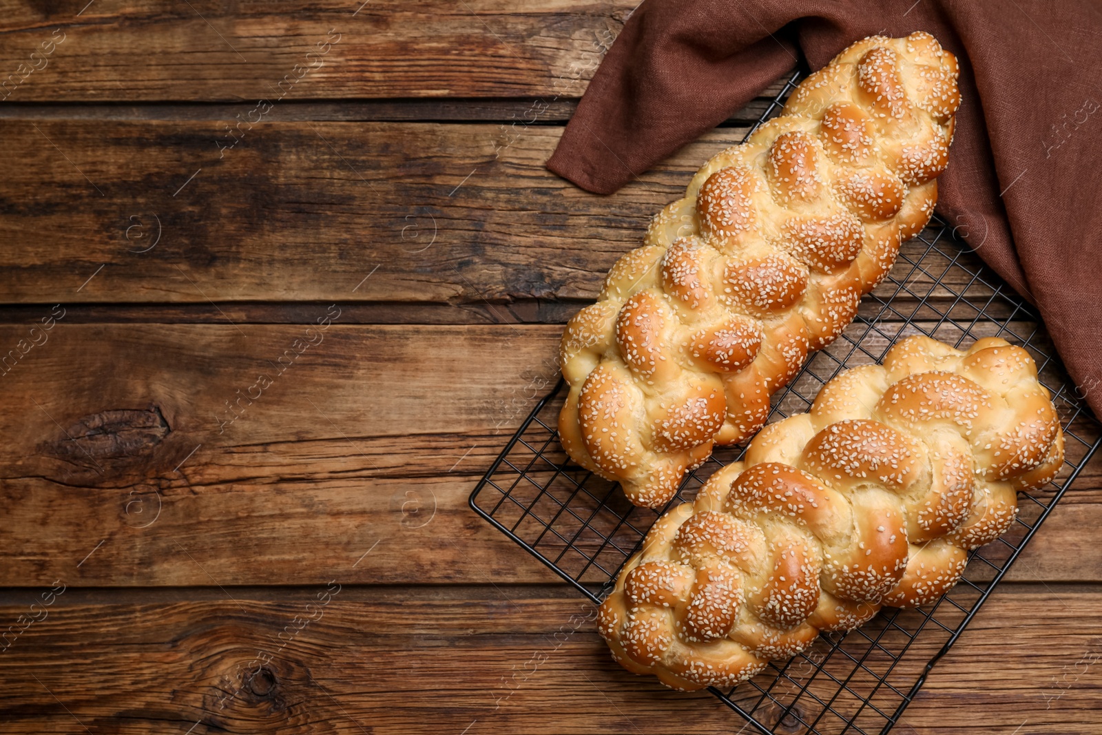 Photo of Homemade braided breads and cooling rack on wooden table, top view with space for text. Traditional Shabbat challah