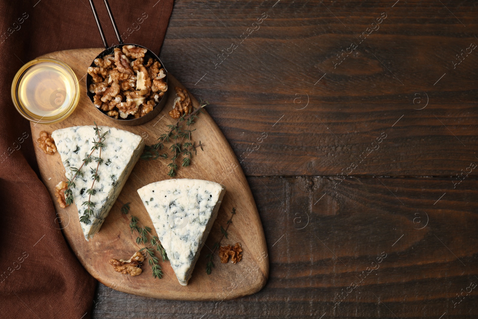 Photo of Tasty blue cheese with thyme, honey and walnuts on wooden table, top view. Space for text