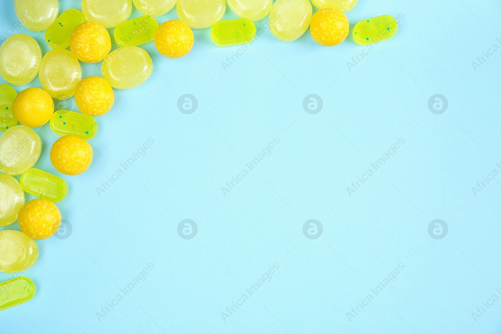 Photo of Delicious lemon candies on light blue background, flat lay. Space for text